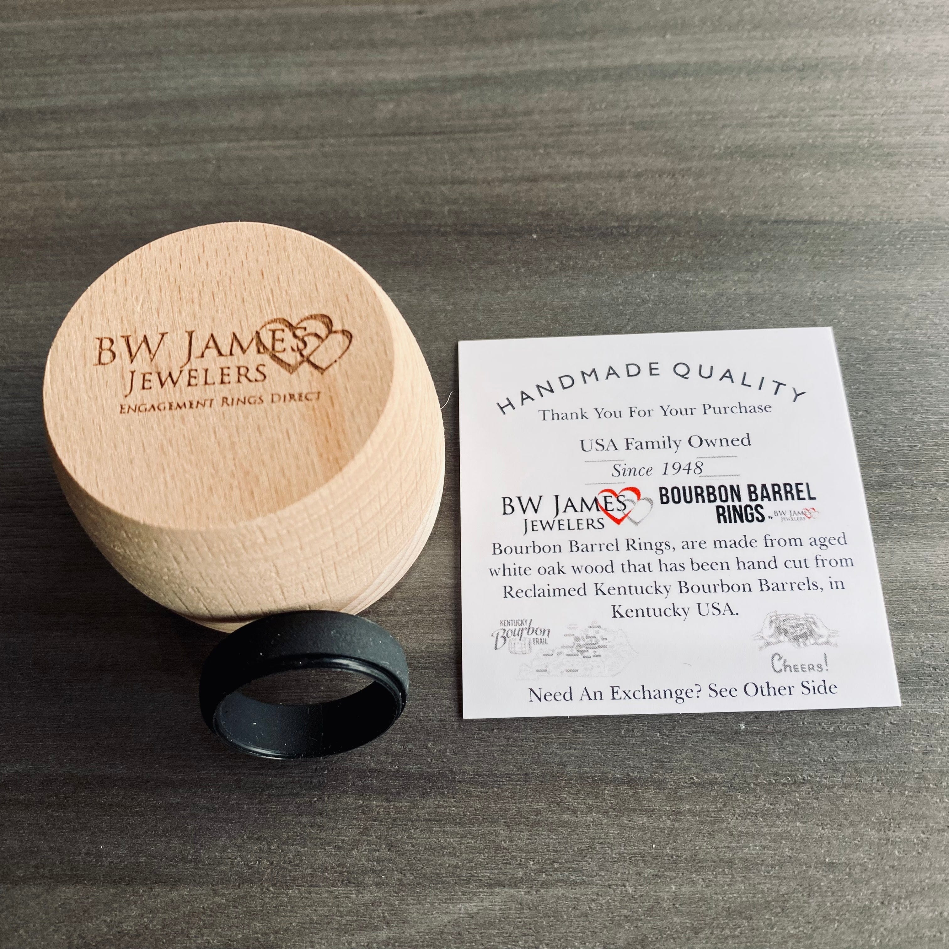 Engagement ring box with a black ring and information card about bourbon barrel rings.