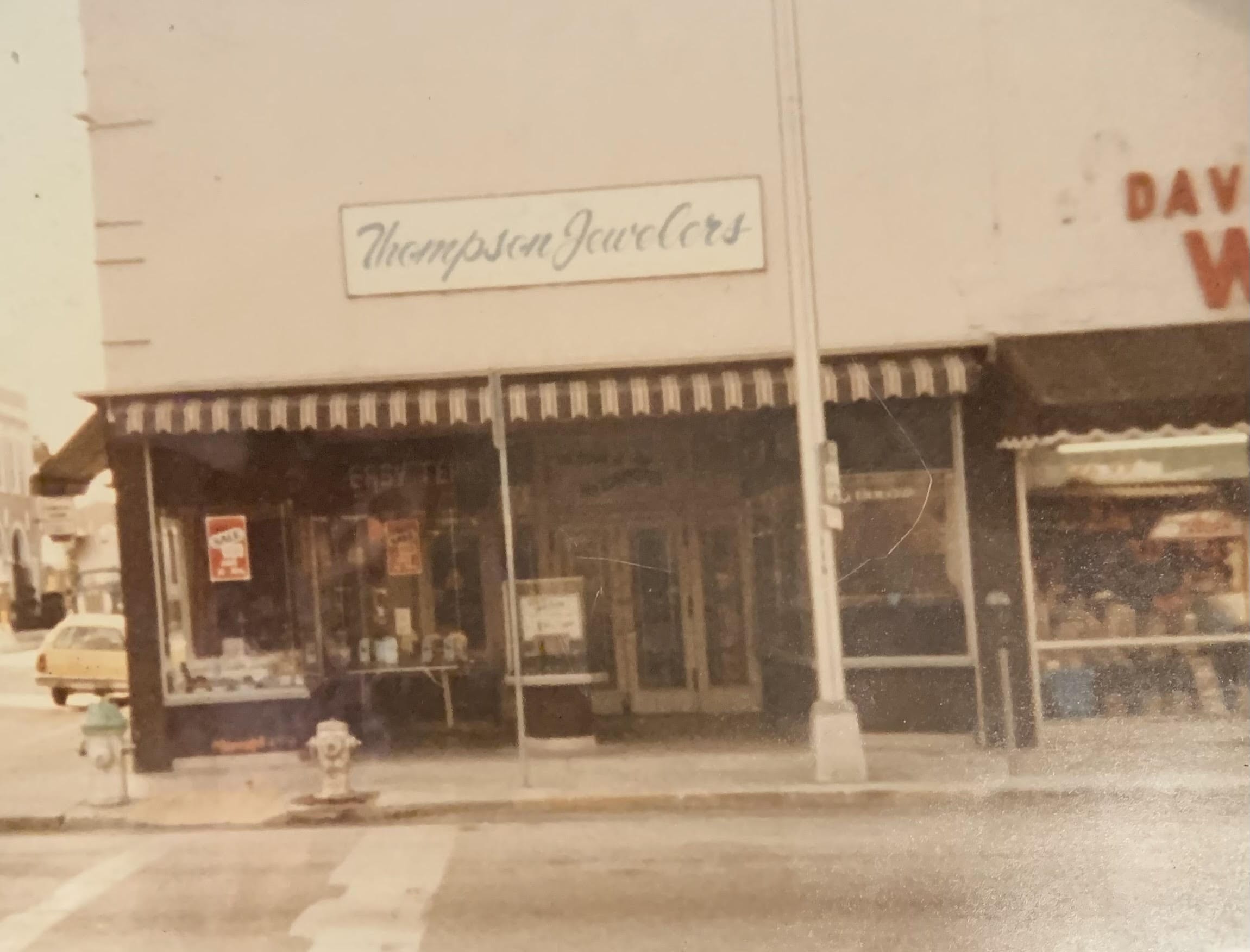 Thompson Jewelers storefront with window displays, striped awning, and nearby shops.
